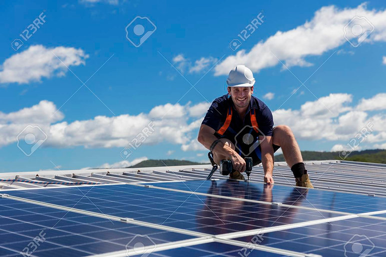 99948747-solar-panel-technician-with-drill-installing-solar-panels-on-roof-on-a-sunny-day.