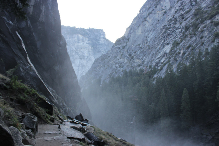 A photo of a narrow rock path, surrounded by high cliffs on all sides and mist rising from the gorge below.