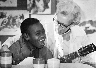 Older white woman singing with young black boy who has disabilities.