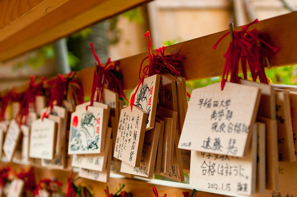 Ema wish plates hang in a temple, adorned with heartfelt messages and illustrations, tied with red strings, symbolizing hopes and prayers.