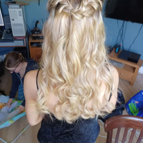 A woman with long, wavy blonde hair styled elegantly with braids stands in a room with a computer and TV