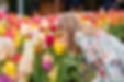 A young girl in a floral dress leans in to smell vibrant tulips