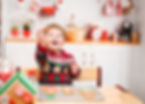 A cheerful child in a festive sweater holds a decorated cookie in a cozy kitchen, surrounded by Christmas-themed treats and decor, exuding holiday joy