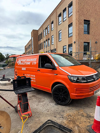 Bright orange van with "Point Drainage Solutions Ltd" parked at a construction site