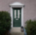 Green front door with decorative glass panels set in a textured, light grey wall