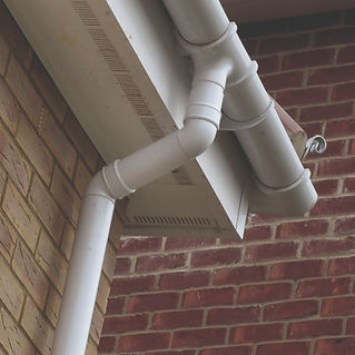 White guttering and downpipe system fixed to brick wall