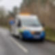 A roadwork service van with flashing amber lights is parked on a tree-lined rural road