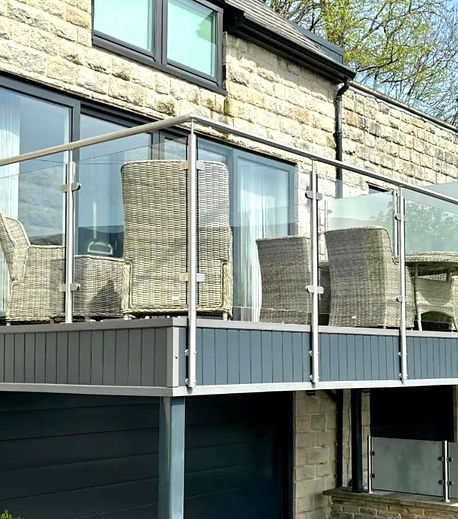 Outdoor balcony with glass railing and wicker chairs, adjacent to a stone building