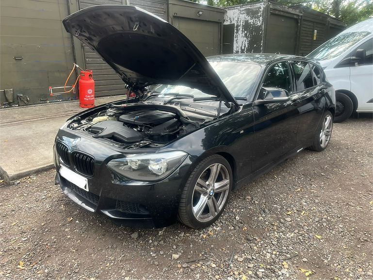 A black car with its hood open is parked outside