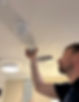 A person installs a smoke detector on a white ceiling, surrounded by other fixtures