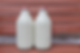 Two glass bottles of milk with red caps stand side by side against a reddish-brown wooden background