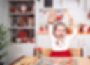 A smiling young girl in a festive kitchen holds up an oven mitt and wooden spoon
