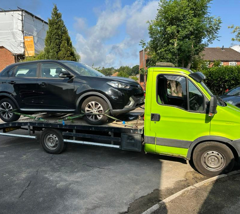 Green recovery vehicle towing a black car