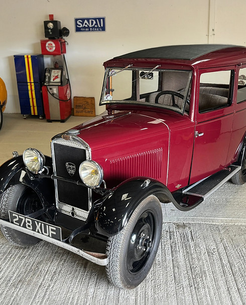 A vintage red car with a boxy shape and black fenders is parked in a garage