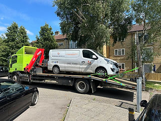 A white van is secured on a bright green tow truck in a residential area