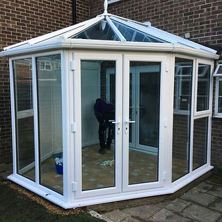 Glass conservatory attached to brick house with patio doors