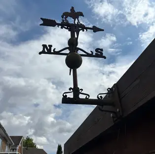 Weather vane with a horse and rider silhouette against a partly cloudy sky