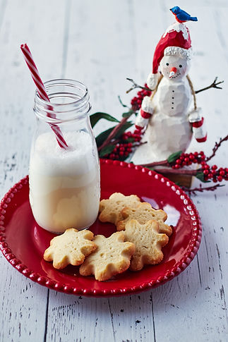 Festive scene with a red plate holding snowflake cookies and a milk bottle with a striped straw
