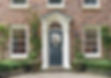 Classic brick house facade with a blue front door, white columns, and arch window
