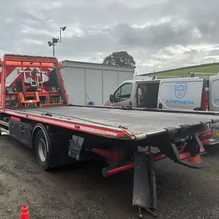 Flatbed truck and two white vans parked on a gravel lot