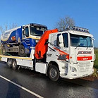 A large white tow truck with a red crane is parked on a road under a clear blue sky