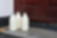 Three glass milk bottles with silver caps sit on the doorstep of a wooden door