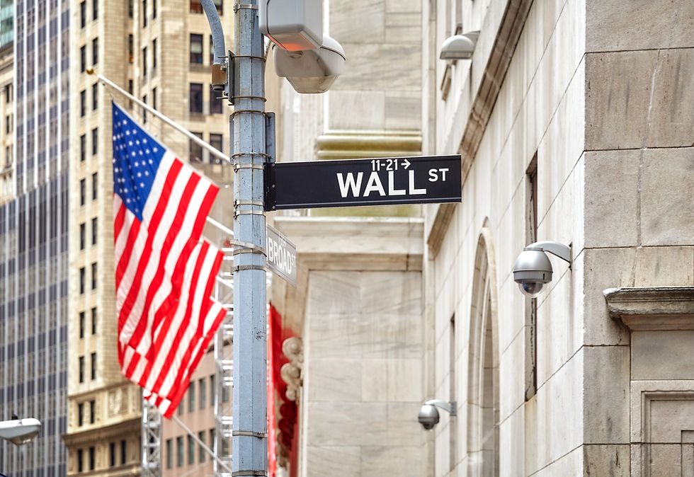 Wall Street sign on a gray building; American flag in background. Busy city feel, security cameras visible, indicating financial district.
