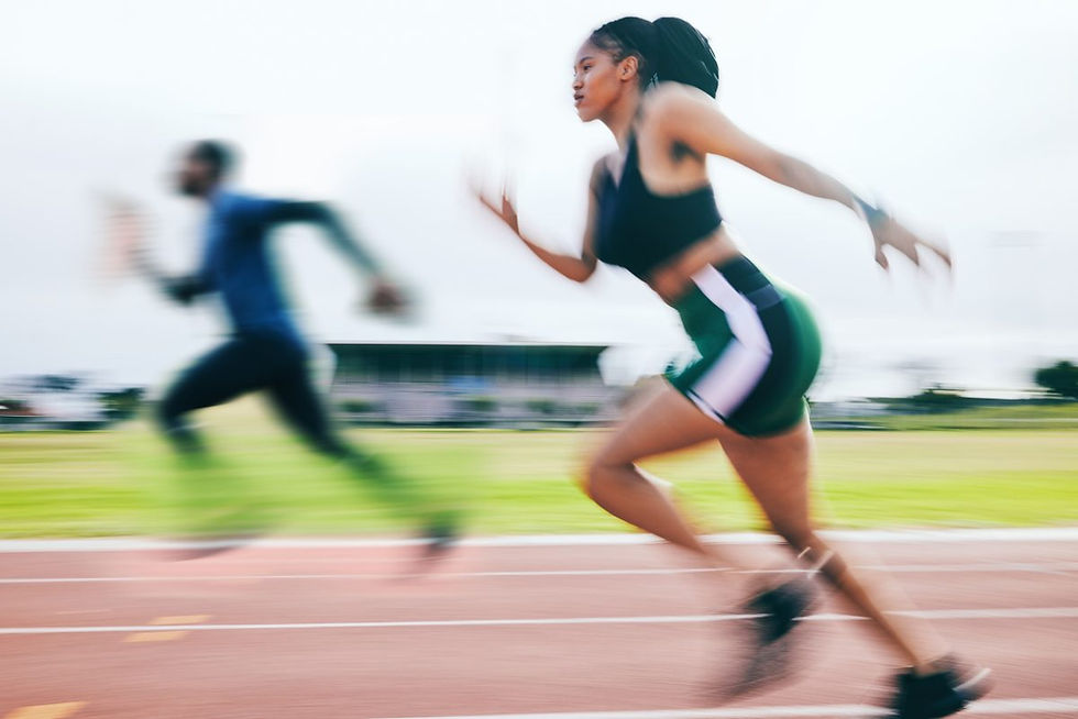 Two athletes sprint on a track, one in focus wearing green and black, the other blurred.