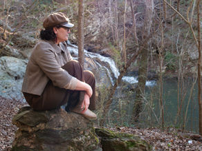 Woman sitting on a rock in a sun beam in front of a waterfall