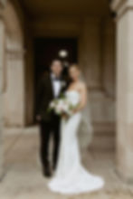 Wedding couple standing together outside under a stone archway 