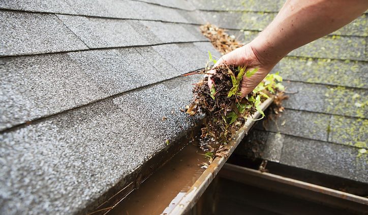 A man pulling out leaf debris from a clogged gutter