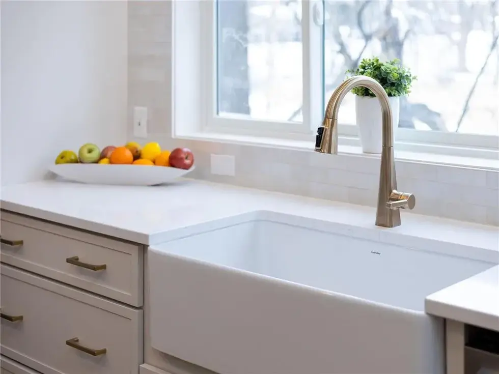 Close up of farmhouse style kitchen sink with gold faucet and tile backsplash
