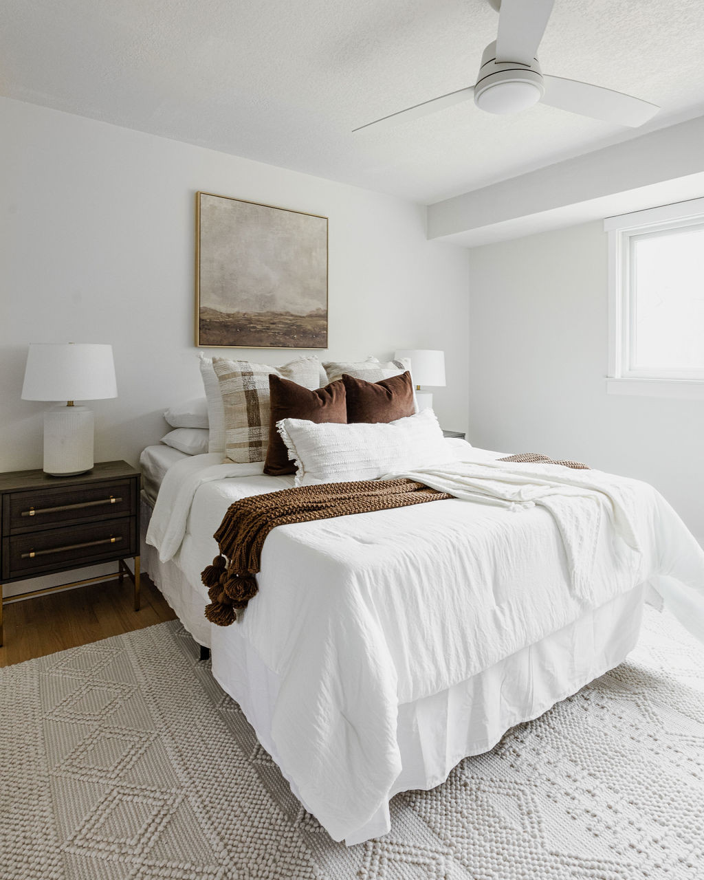 Modern bedroom with white bedding, brown accents, and abstract art