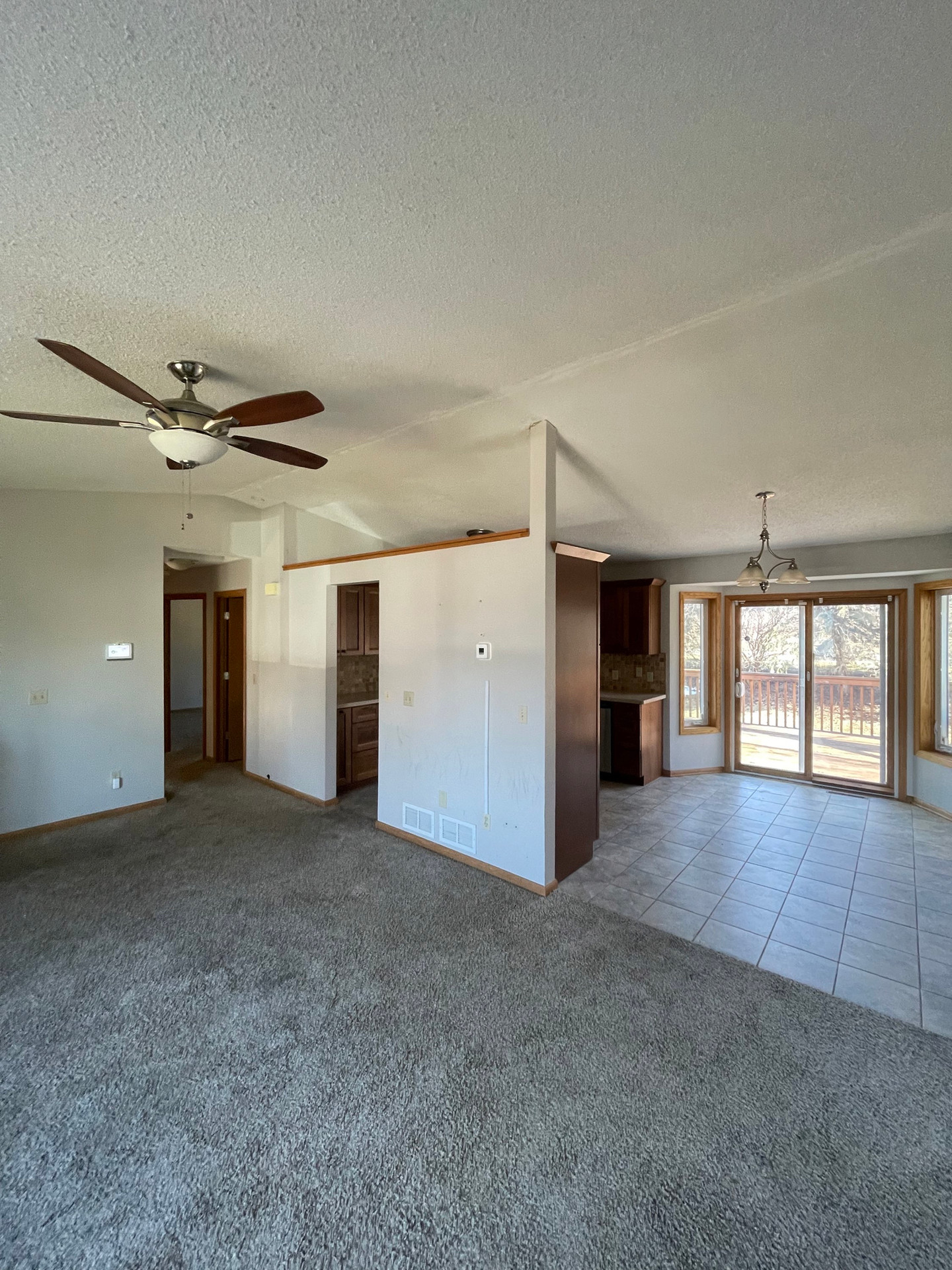 Empty living room with ceiling fan, opens to kitchen