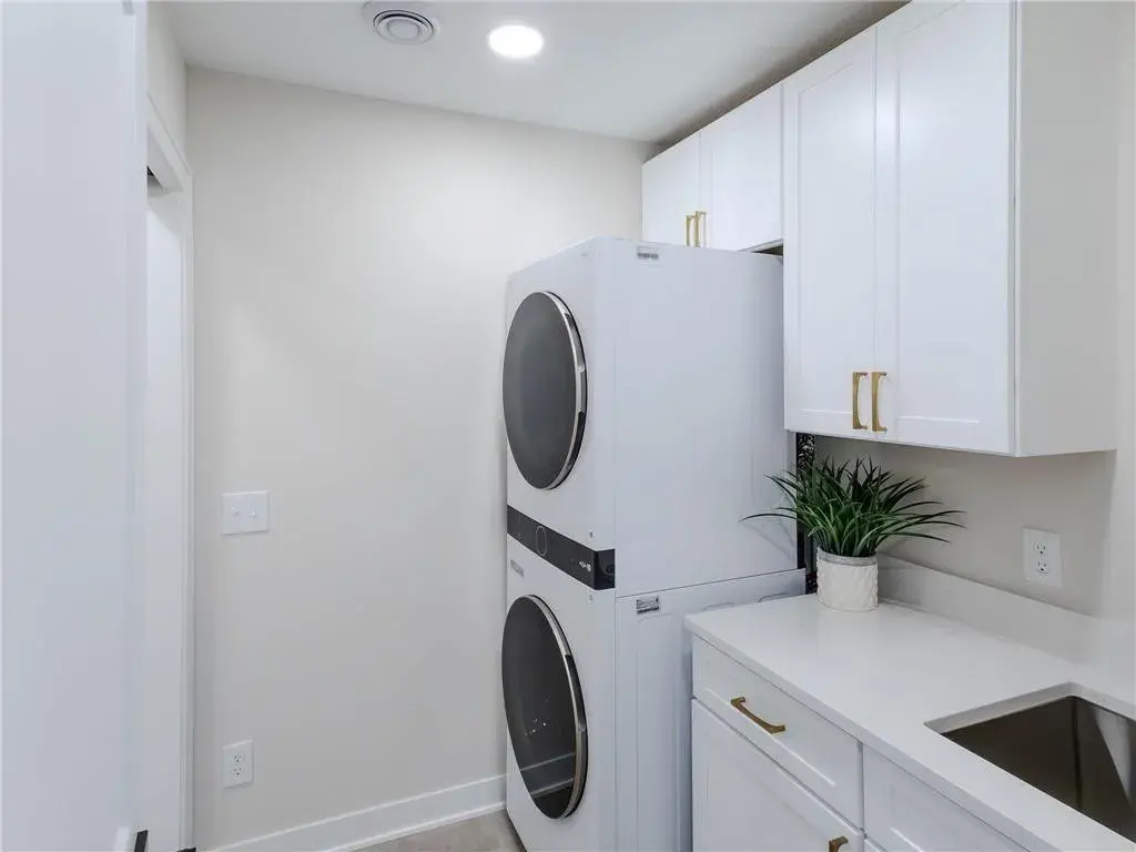 laundry room with white stacked washer and dryer, white cabinetry and gold hardware