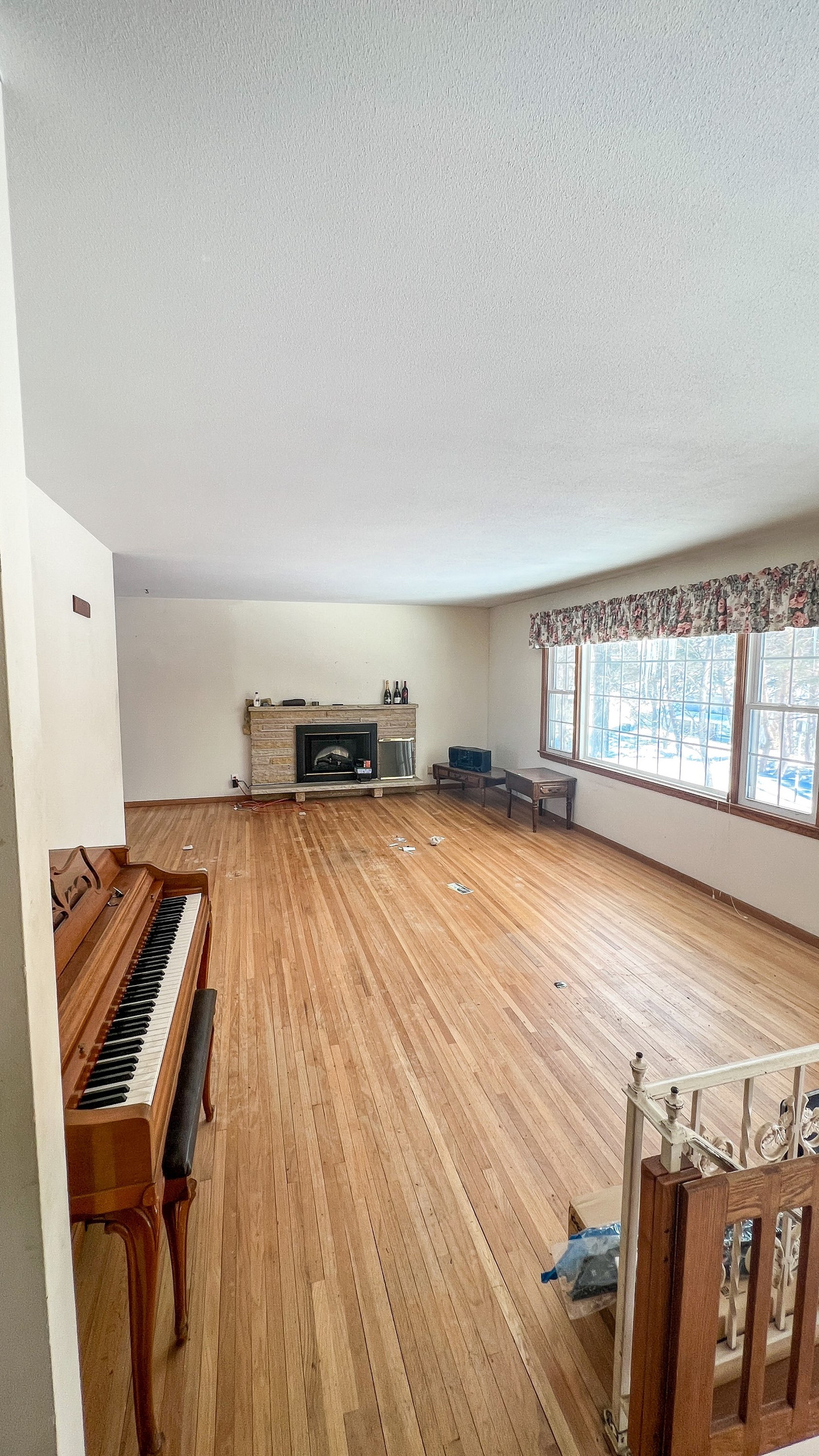 Empty living room with fireplace, hardwood floors, and piano