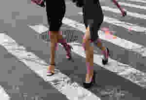 Two women crossing the street at the cross-walk, in black high heels and black skirts.
