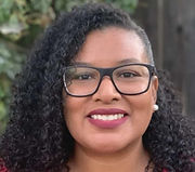 Woman of mixed-race ethnicity (Black/African American and Mexican American) with curly hair, wearing a pink shirt and glasses.
