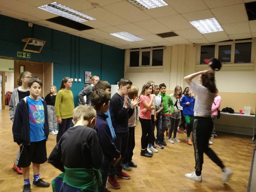 A group of young people face another young person. They are clapping and listening to what she says.
