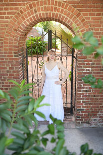 Senior picture of a blonde girl in a white dress against a brick arch surrounded by leaves. Key West senior photos.