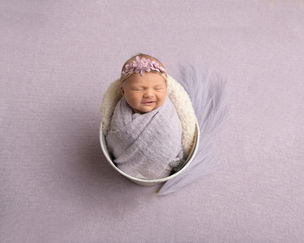 Beautiful baby girl in lavender in a bucket swaddled and smiling with some feathery flowers beside her. Key West newborn photography studio.