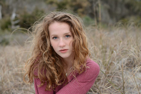 Red head senior in a mauve sweater sitting in the wheat colored grasses in Myrtle Beach.