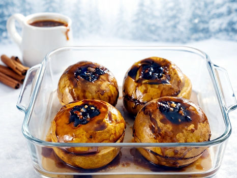 Cztery jabłka pieczone z sosem toffi w szklanym naczyniu, obok w kubeczku sos toffi zimą.