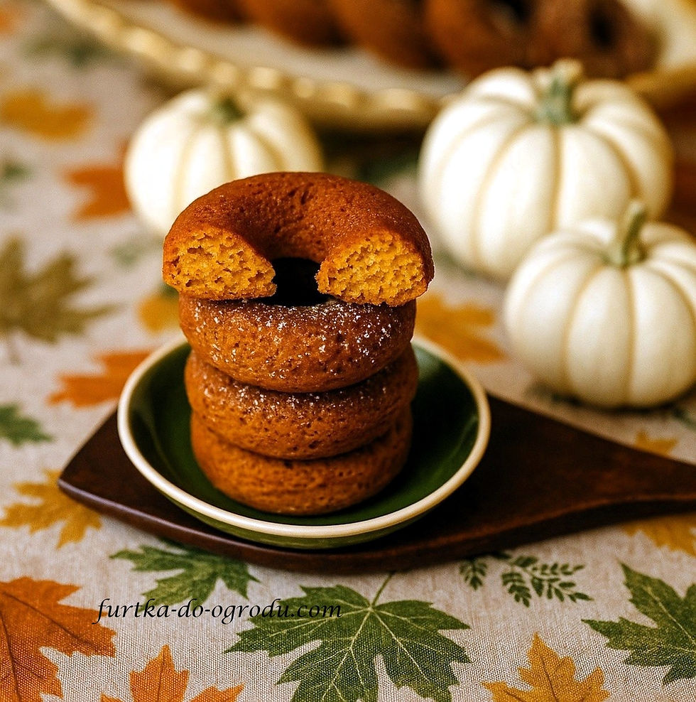 Napoczęty donat, ułożony na donatach dyniowych z dekoracyjnymi, białymi dyniami ułożone na obrusie w jesienne listki.