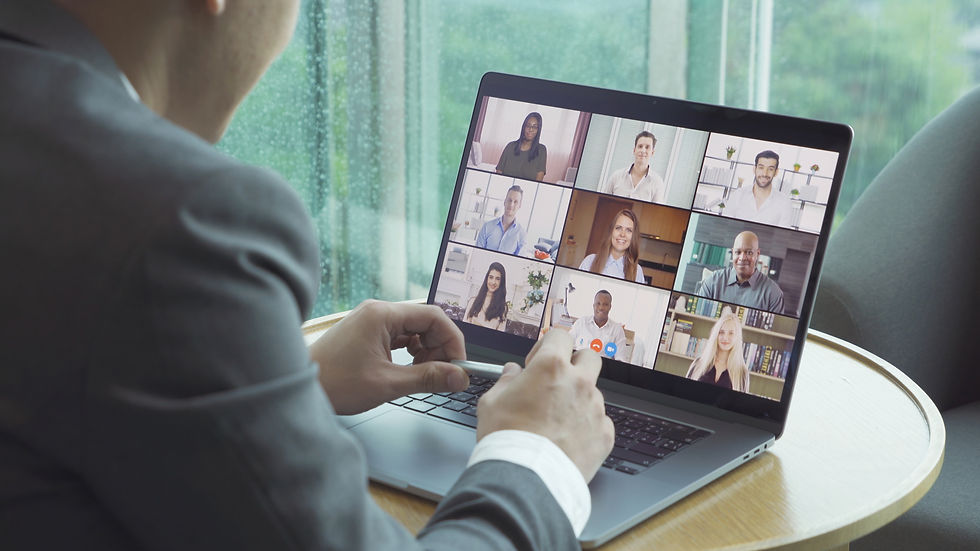 Person in a suit on a video call with nine people, displayed on a laptop. Window view of a rainy day in the background.