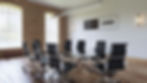 A stylish virtual conference room with exposed brick walls, black leather chairs, a glass-top table, and custom logo placemen