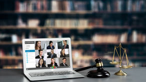Laptop showing a video conference with nine people in a library setting. A judge's gavel and scales of justice are on the desk.