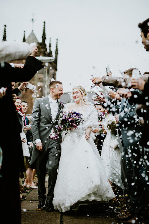 real bride and groom walking through a line of guests who are throwing lots of confetti