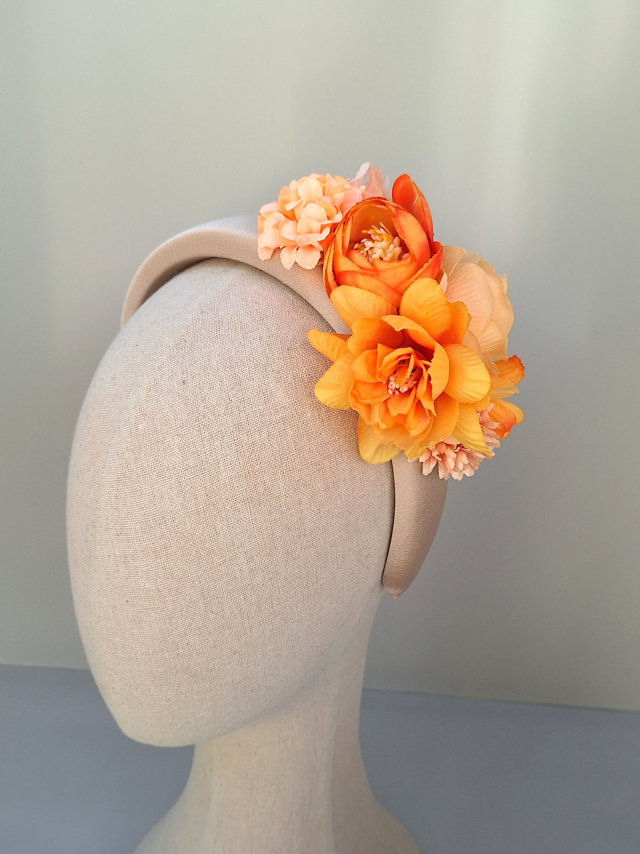 Burnt orange and peach floral headband on mannequin, perfect for wedding guests or mothers of the bride.