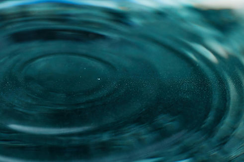 Concentric ripples spread across a body of teal blue water, macro shot.